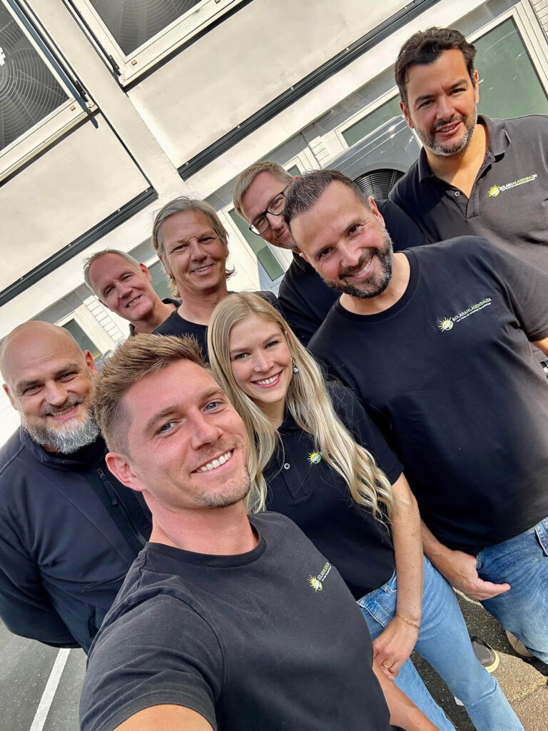 Marcel Klangwart mit einem Teil seines Teams. Er, sechs weitere Männer und eine Frau lächeln in die Kamera, die Marcel hält. Alles Experten aus den Abteilungen MArketing, Kundenberatung und den Handwerksbereichen